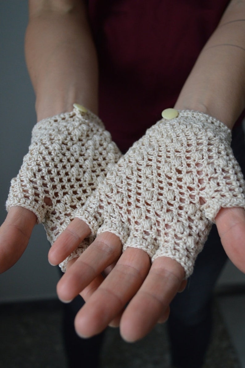 Peut inclure: Une paire de mitaines en crochet beige avec un bouton sur chaque poignet.