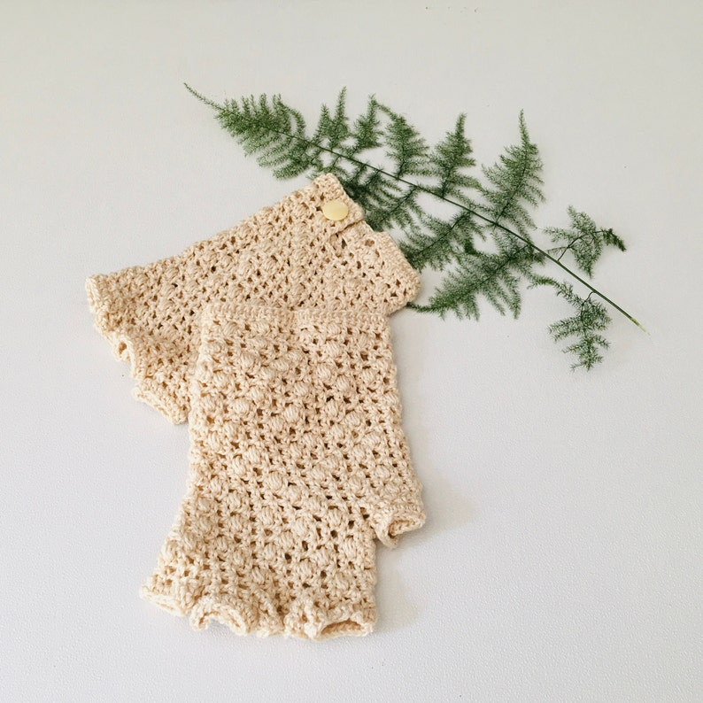 Peut inclure: Une paire de mitaines en crochet de couleur cr&egrave;me avec un seul bouton sur le dessus d'une mitaine.