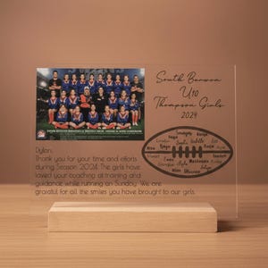 May include: A clear acrylic plaque on a wooden base featuring a team photo of the South Barwon U10 Thompson Girls 2024. The plaque includes a football graphic with signatures, and a printed message thanking a coach named Dylan for the season.