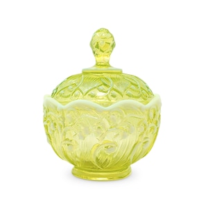 May include: A translucent yellow glass sugar bowl with a matching lid, featuring an intricate embossed floral pattern across the body and lid, a scalloped upper rim, and a decorative finial handle on top of the rounded lid structure.