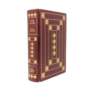 May include: A hardcover book titled "Tom Jones" by Henry Fielding, from The Franklin Library. The book has a burgundy leather cover with gold decorative accents and lettering. The spine and cover feature ornate gold patterns.