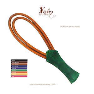 May include: A leather paddle with a green handle and orange loop. The text "BRAT LOOP LEATHER PADDLE" is visible. The image also shows a color chart with options like black, dark brown, and orange. The text "100% HANDMADE IN EUROPE, LATVIA" is also visible.
