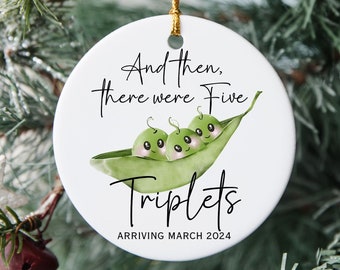 May include: A white ceramic Christmas ornament with a gold string. The ornament features the text "And then, there were Five Triplets ARRIVING MARCH 2024" above a watercolor illustration of three peas in a pod.