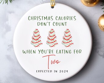 May include: White ceramic Christmas ornament with the text "Christmas Calories Don't Count When You're Eating For Two Expected in 2024". Three gingerbread Christmas trees are illustrated on the ornament.