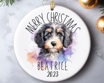 May include: White ceramic Christmas ornament with a watercolor painting of a black and white puppy with a purple, blue, and orange background. The ornament says "Merry Christmas Beatrice 2023" in black text.