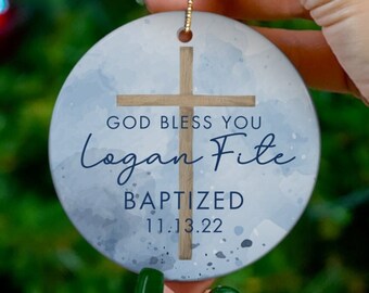 May include: A blue and white watercolor-style Christmas ornament with a wooden cross and the text "God Bless You Logan Fite Baptized 11.13.22"