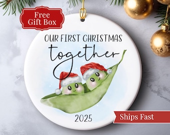 May include: A white ceramic Christmas ornament with the text "OUR FIRST CHRISTMAS together 2025". The ornament features two pea pod characters wearing Santa hats. A red banner reads "Free Gift Box".