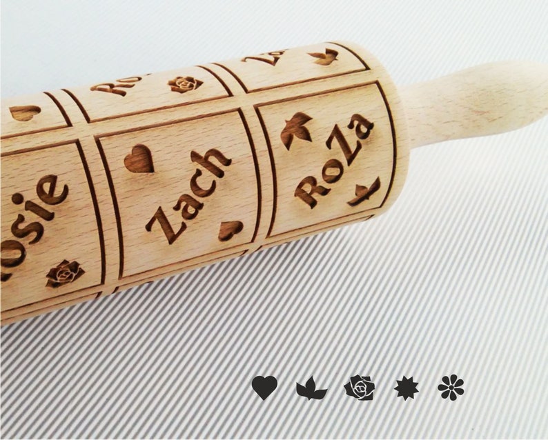 K&ouml;nnte beinhalten: Ein Holz-Nudelholz mit den Namen "Rosie", "Zach" und "Roza" eingraviert. Das Nudelholz hat auch Herzen und Blumendesigns eingraviert.