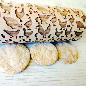 以下が含まれることがあります： 鶏とひよこの彫刻が施された木製麺棒。同じデザインが刻まれた丸いクッキーが3つある。