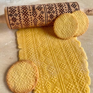 May include: A wooden rolling pin with a geometric pattern engraved into the surface. The rolling pin is used to create patterned cookies. The cookies are light yellow and have the same geometric pattern as the rolling pin.