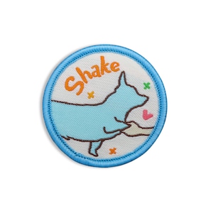 May include: A blue and white embroidered patch with a cartoon dog shaking its paw. The patch has the word "Shake" embroidered in orange on it.