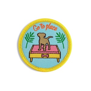 May include: A yellow embroidered patch with a blue background featuring a dog standing on a pink and yellow dog bed. The text "Go to place" is embroidered in orange and yellow on the patch.