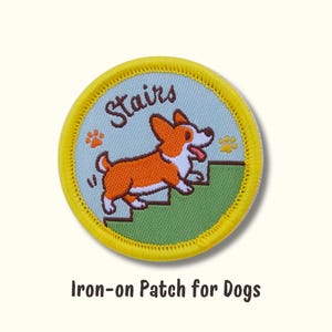 May include: Round iron-on patch featuring a cartoon corgi dog climbing stairs. The patch has a light blue background with the word "Stairs" and paw prints. The border is yellow. Text at the bottom reads "Iron-on Patch for Dogs".
