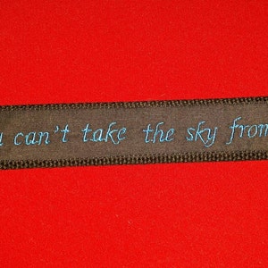 May include: Black ribbon with the text "You can't take the sky from me" embroidered in blue thread.