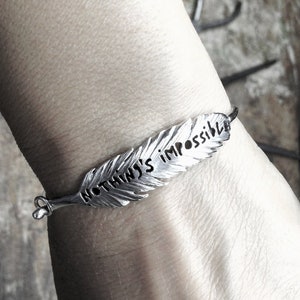 May include: A silver feather bracelet engraved with the words "Nothing's Impossible".