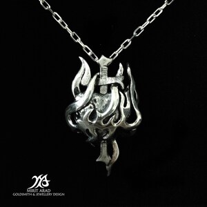 Op de afbeelding: Een zilveren ketting met een hanger met een hart dat door een zwaard wordt doorboord, omringd door vlammen. De hanger is bevestigd aan een zilveren ketting.