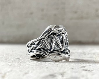 Può includere: Un anello d'argento con un design testurizzato e organico. L'anello è realizzato in un unico pezzo di metallo e ha una forma unica e fluida.