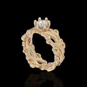 Könnte beinhalten: Ein goldener Ring mit einem filigranen, komplizierten Design, das mit einem einzigen, runden, klaren Edelstein in der Mitte verziert ist.