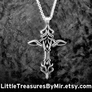 May include: A silver chain necklace with a detailed silver cross pendant. The cross has a floral design and is intricately crafted. The necklace is hanging against a dark textured background.