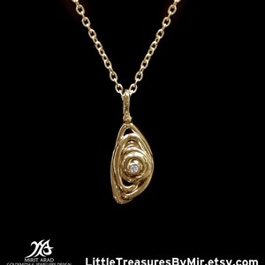 Puede incluir: Un collar de oro con un colgante que presenta un diseño en espiral y un pequeño diamante en el centro.