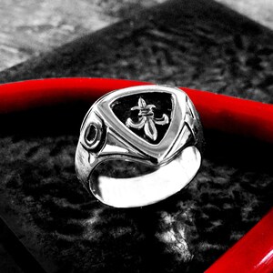May include: A silver ring with a triangular design featuring a fleur-de-lis symbol. The ring is on a black and red surface.  LittleTreasuresByMir.etsy.com