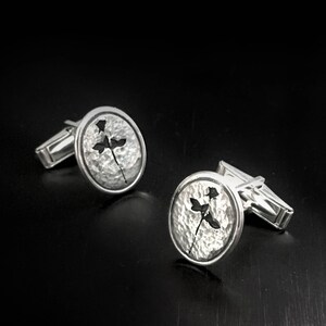 May include: A pair of silver cufflinks with a hammered finish and a delicate floral design. The cufflinks are round and have a polished edge.
