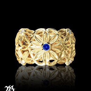Puede incluir: Un anillo de oro con un zafiro azul y diamantes blancos engastados en un diseño floral.