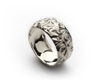 Puede incluir: Un anillo de plata con un intrincado diseño floral. El anillo es ancho y tiene un acabado liso y pulido.