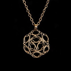 Pode incluir: Um colar de ouro com um delicado e intrincado pingente com um design circular com um padrão repetitivo de laços e curvas.