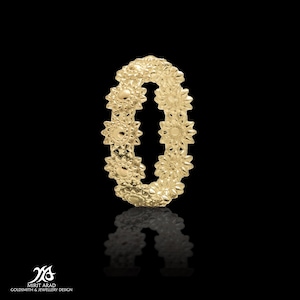 Puede incluir: Un anillo de oro con un delicado diseño de pequeñas flores alrededor de la banda.