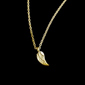 Könnte beinhalten: Eine goldene Kettenkette mit einem kleinen goldenen Flügelanhänger. Die Kette liegt auf einem schwarzen Hintergrund.