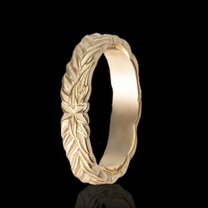 Puede incluir: Un anillo dorado con un diseño detallado de hojas y estrellas. El anillo tiene una superficie texturizada y un interior liso. El anillo se muestra sobre un fondo negro. El anillo es una joya.
