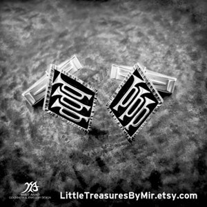 May include: A pair of silver cufflinks with a black enamel design. The design features a stylized letter "P" repeated three times.
