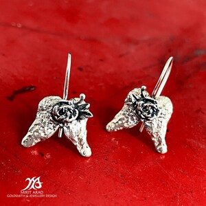 Puede incluir: Pendientes de plata con diseño de alas texturizadas y un pequeño detalle de rosa.