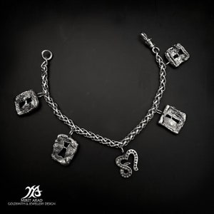Könnte beinhalten: Ein silbernes Kettenarmband mit fünf Anhängern, darunter ein Herz, ein Schlüsselloch und drei quadratische Anhänger. Die Anhänger sind alle strukturiert und haben einen leicht gealterten Look.