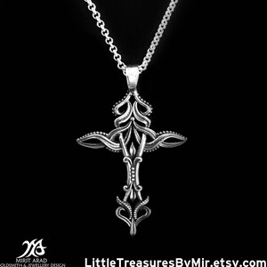 May include: A silver pendant necklace with a detailed cross design. The cross is ornate and features intricate details. The chain is silver and has a delicate design.