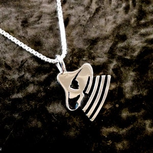 May include: A silver necklace with a pendant featuring a stylised silhouette of a person wearing a hat. The pendant has a striped design.
