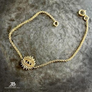 Pode incluir: Um bracelete de corrente de ouro com um pequeno amuleto de olho turco. O amuleto é feito de ouro e tem uma pedra azul no centro.