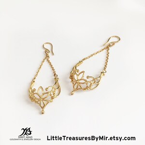 K&ouml;nnte beinhalten: Goldene Ohrringe mit einem filigranen Blumenmuster. Die Ohrringe haben eine Kette mit einer kleinen Blume am unteren Ende.