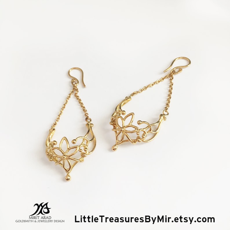 K&ouml;nnte beinhalten: Goldene Ohrringe mit einem filigranen Blumenmuster. Die Ohrringe haben eine Kette mit einer kleinen Blume am unteren Ende.