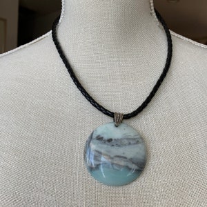 May include: A black leather cord necklace with a large round pendant made of green, white, and gray marbled stone.