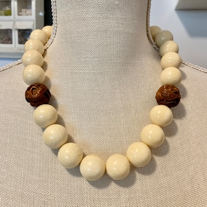 May include: A white ivory bead necklace with two brown carved beads. The necklace is on a white mannequin.