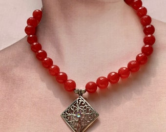 May include: A red beaded necklace with a silver filigree pendant featuring a clear crystal in the center.