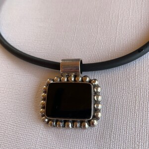 May include: A black onyx pendant necklace with a silver frame and a black cord.