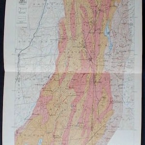 May include: A folded geological map of Eastern New York and Western Vermont, featuring a detailed depiction of the region's geological formations. The map uses a color-coded system with pink, yellow, and blue hues to represent different rock types and geographical features.