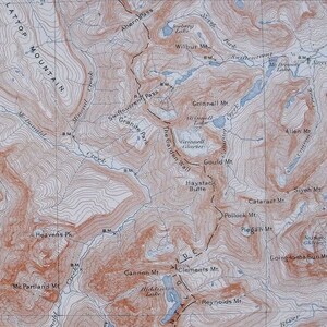 May include: A detailed topographic map with contour lines, featuring mountain ranges, lakes, and trails. The map uses brown and blue hues, with place names like Grinnell Mt. and Hidden Lake. It is a vintage map.