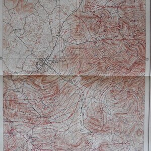 May include: A vintage topographic map with contour lines in red and black, depicting a detailed landscape. The map shows roads, towns, and geographical features. The map is folded and has a cream-colored background.