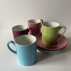 Puede incluir: Cuatro tazas de cerámica coloridas con platillos a juego. Las tazas son en tonos de azul, burdeos, rosa y verde, con interiores blancos. Los platillos son rosas y apilados. Un diseño simple y moderno para la cocina o el comedor.