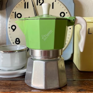 Könnte beinhalten: Ein lindgrüner Espressokocher für den Herd mit weißem Griff und Deckelknopf. Der achteckige obere Teil trägt den weißen Schriftzug La Peppina Made in Italy. Der untere Teil besteht aus unlackiertem, silberfarbenem Metall in achteckiger Form.