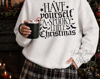 Op de afbeelding: Een wit sweatshirt met lange mouwen en zwarte tekst "HAVE yourself A SPOOKY LITTLE Christmas" met kleine ster- en vleermuisafbeeldingen. Het sweatshirt wordt gecombineerd met een zwart, wit en grijs geruite short.